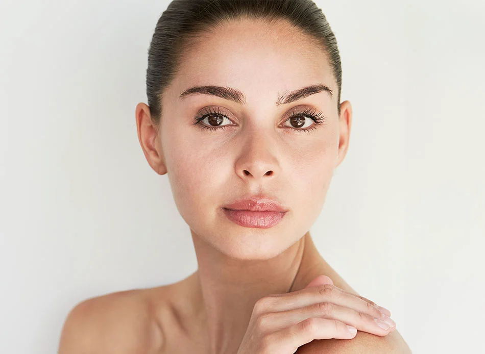 Woman with smooth skin and natural makeup, looking directly at the camera, set against a light background - Eyebrow Transplant in Bethesda, MD