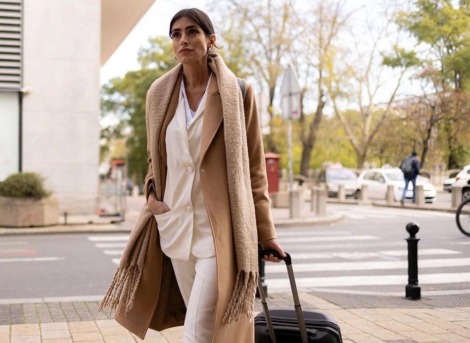 Woman in a long coat and scarf, walking in a downtown, holding her suitcase - Out of Town Patient Resources in Bethesda, MD